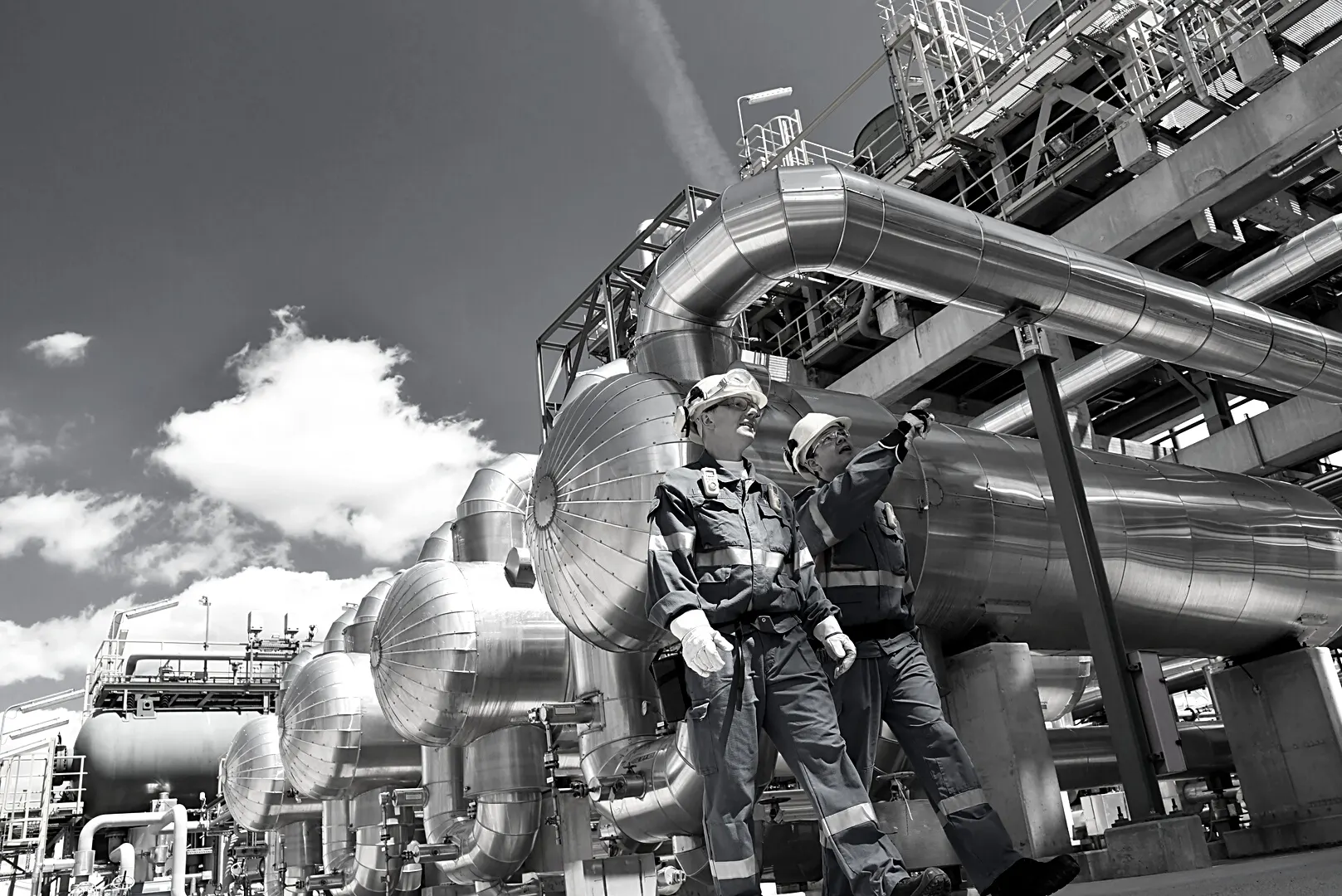 Two engineers in hard hats inspecting pipework at a plant